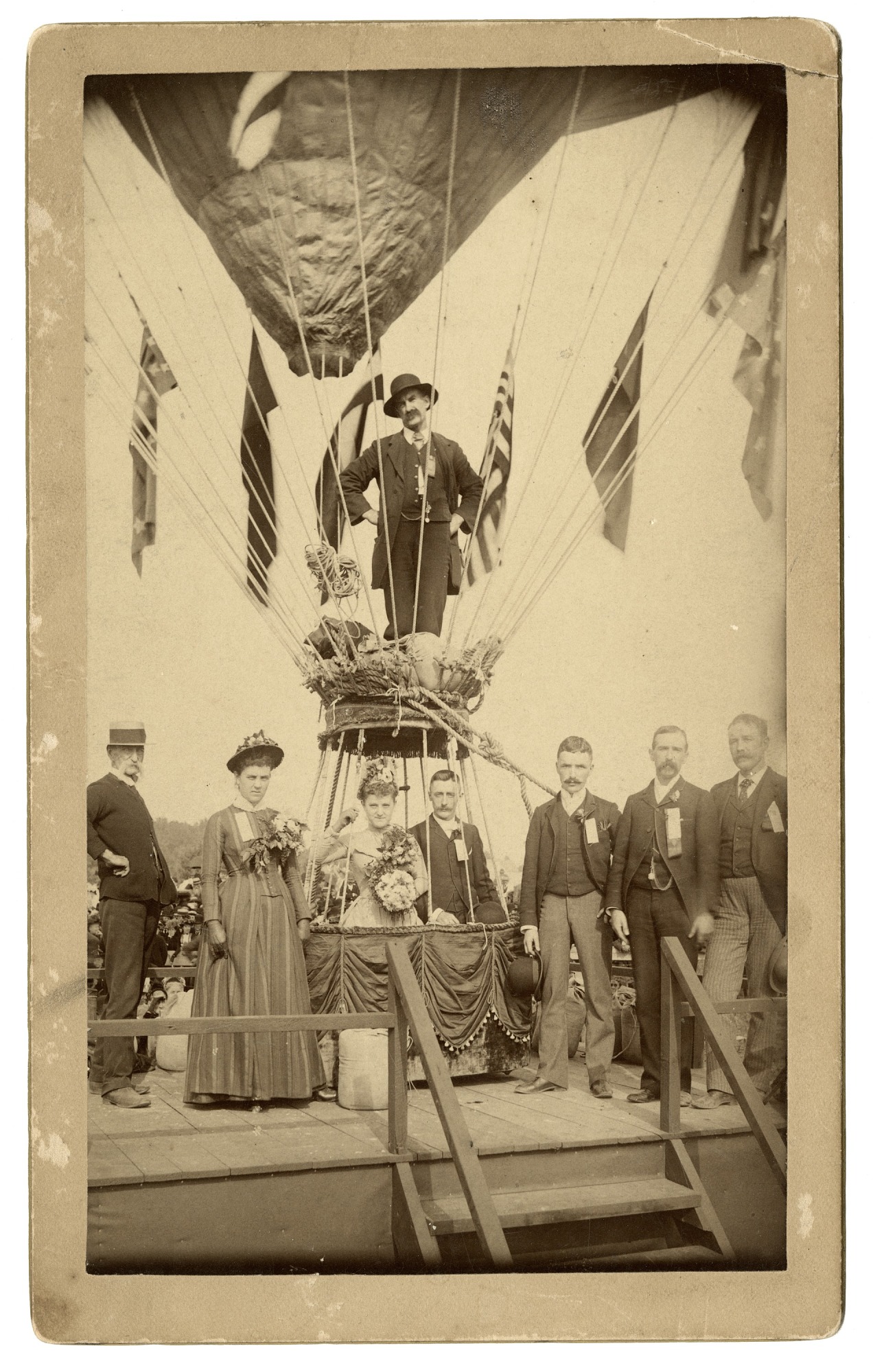 Click to view larger image A group stands at a large balloon. A couple is in the basket, with another man standing above them.