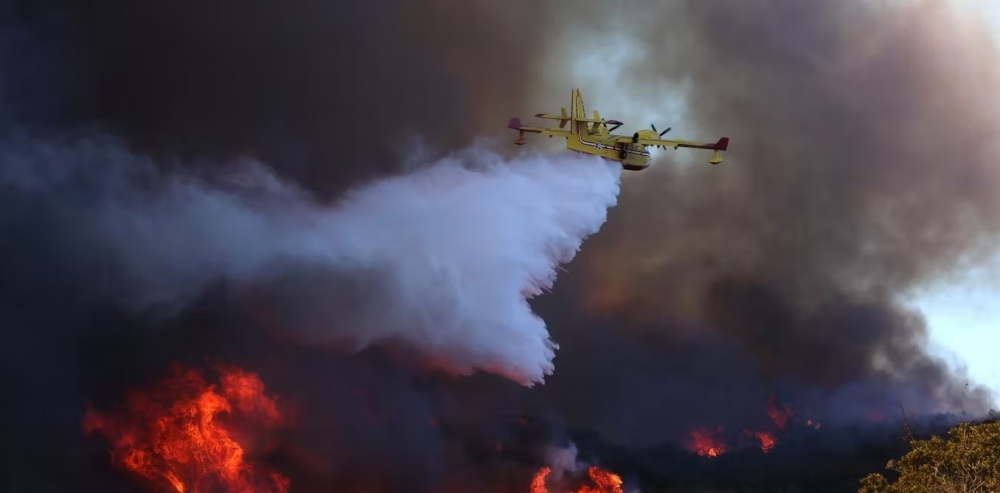 Click to view larger image A plane dumps water onto a burning hillside