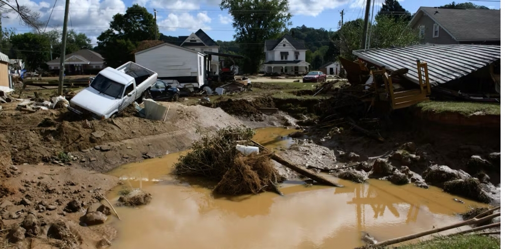 Click to view larger image A big pool of muddy water surrounded by small homes and a white pickup truck that's angled into a ditch.
