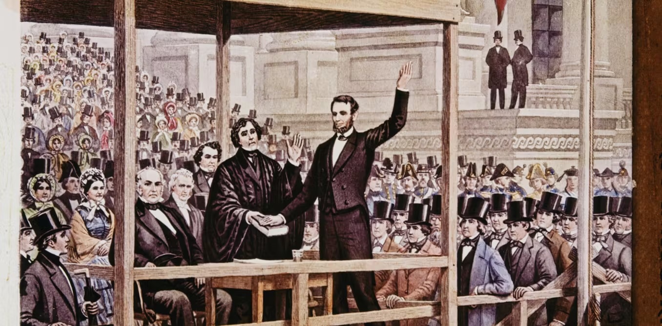 Click to view larger image Two men stand on a wooden platform in front of a crowd of people.