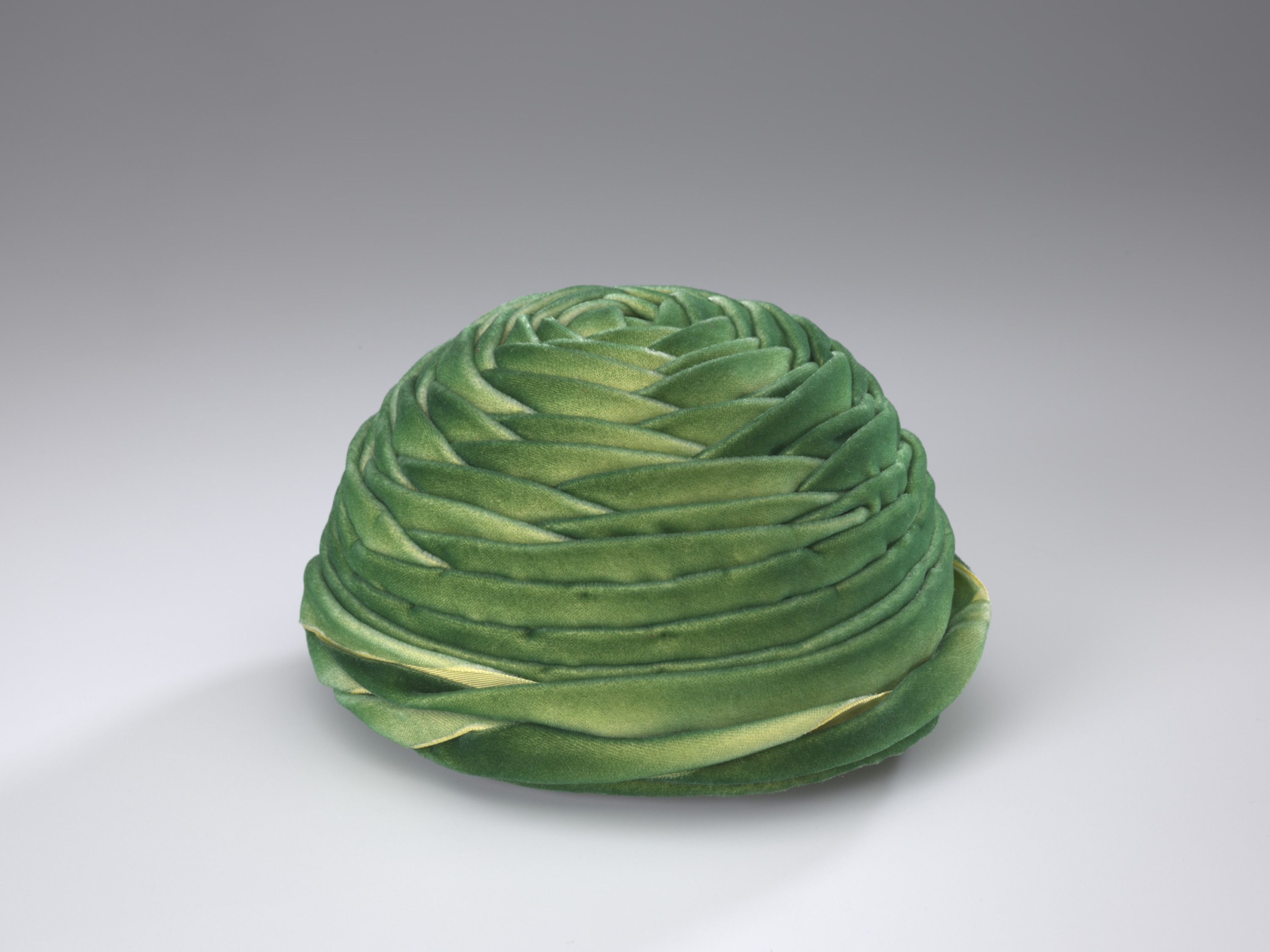 Click to view larger image Green velveteen hat. It is circular with layers of fabric in a wrapped design.