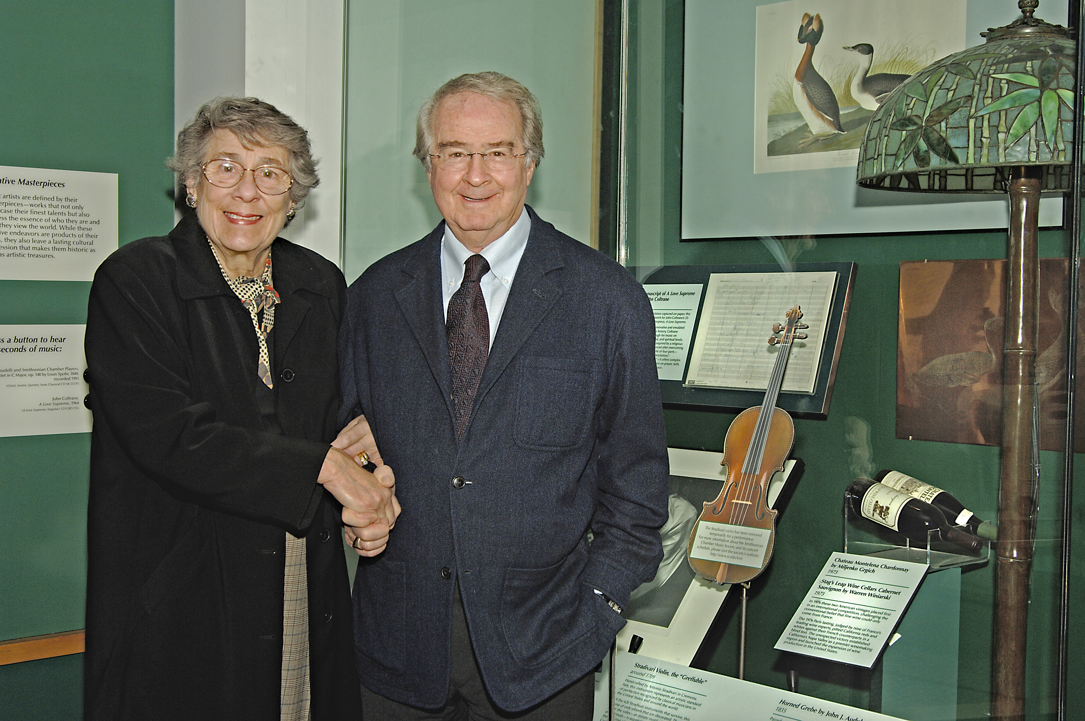 Two people shaking hands in front of a museum exhibit case