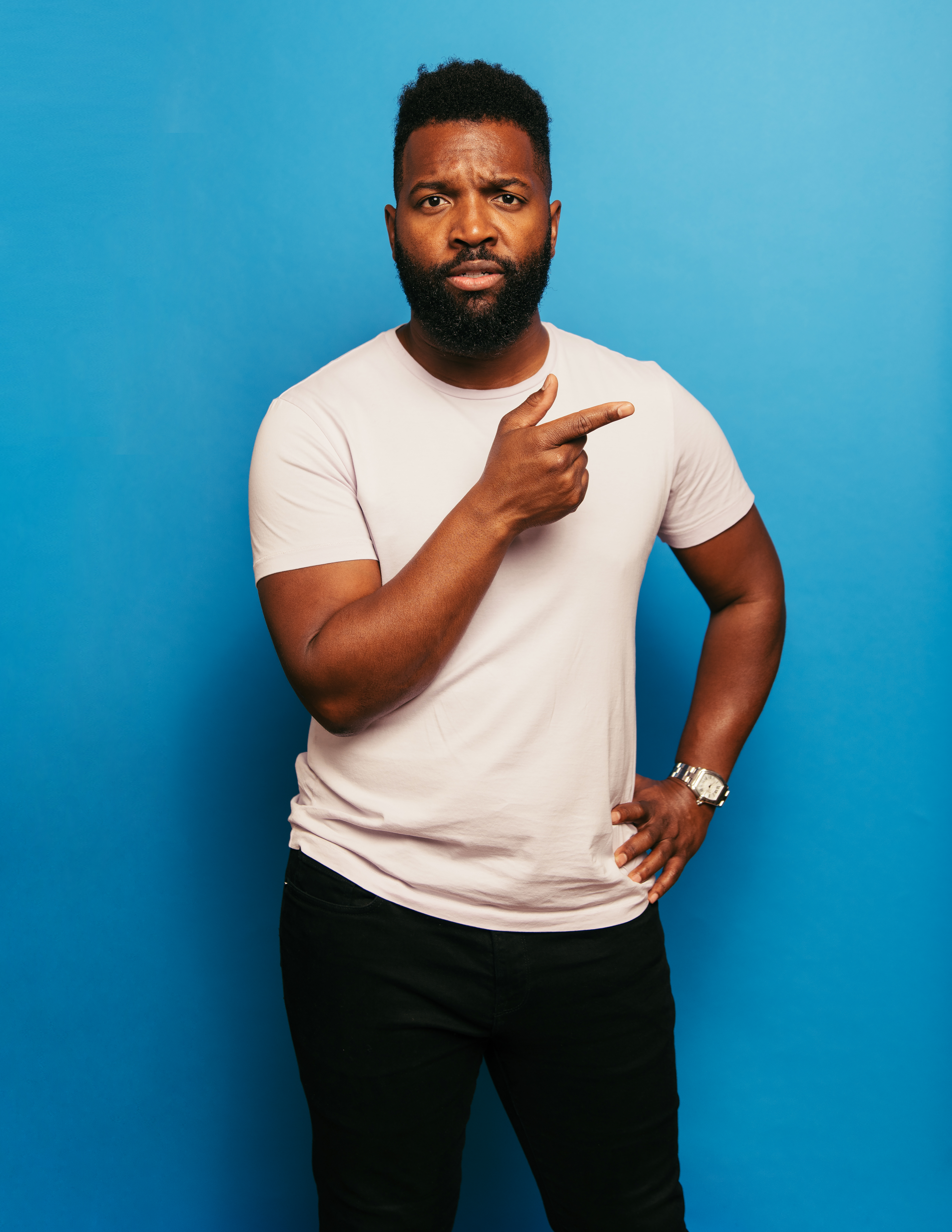 Man stands in front of a solid blue background and looks quizzically ahead