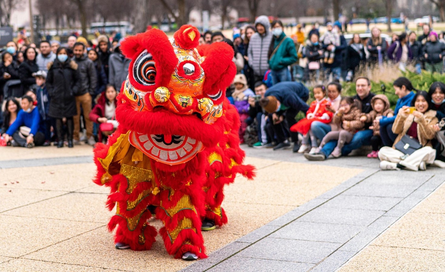 A crowd watching a lion dancer perform outside.