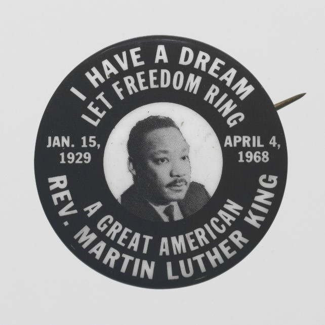 Photograph of black and white pinback button with image of Martin Luther King Jr.s face in center surrounded by quotes.