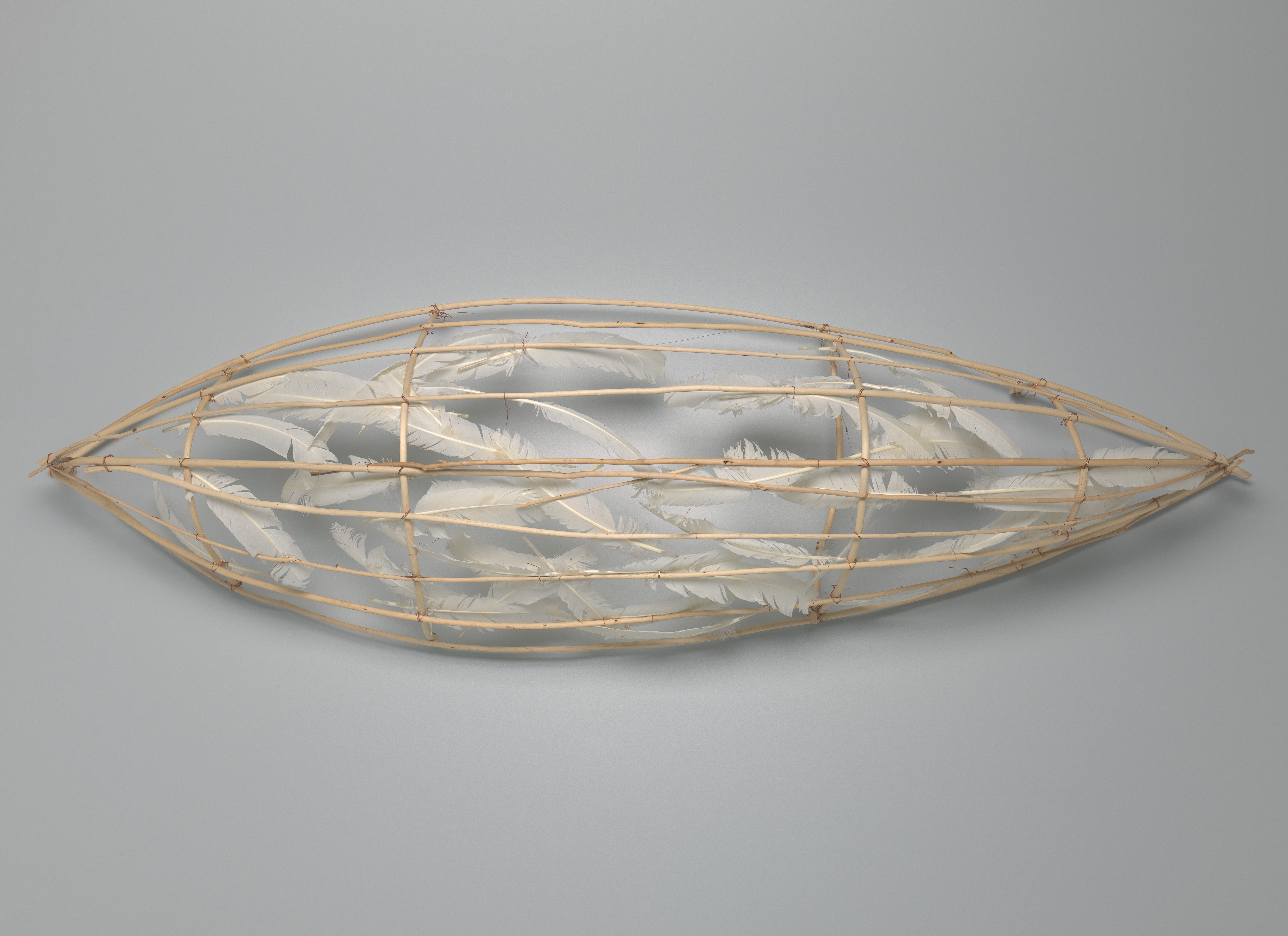 Sculpture in pointed oval shape made out of light wood and white feathers.