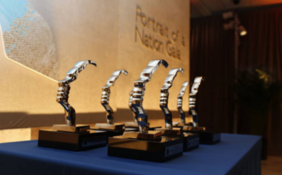 A group of awards with silver hand sculpture and wood base sit on a podium.