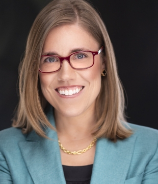 Woman with shoulder-length, light brown hair and glasses smiles for a headshot