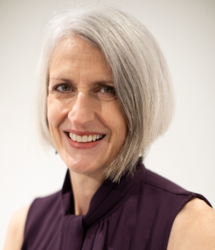 Woman with gray hair and sleeveless purple shirt smiles