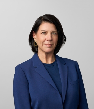 Woman with brunette bob in a deep blue suit smiles toward camera.