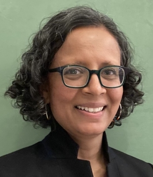 Head shot of Sanchita Balachandran wearing glasses and a dark jacket with pale green background