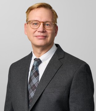 Man with short blonde hair and glasses sits for a shoulder-up portrait.