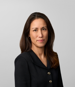 Woman with long brown haur and brown eyes, wearing a black cardigan, smiles toward camera.