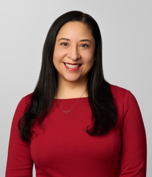 Woman with long black hair in a red dress smiles for a headshot.