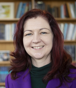 Lisa Kewley sits in front of a bookcase and smiles directly ahead