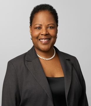 Woman in a dark blazer and pearls smiles toward camera
