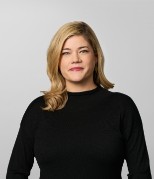 Woman with curled blonde hair wearing a black blouse smiles for a headshot.