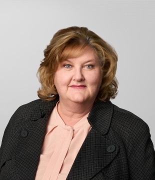 Woman with shoulder-length, curled strawberry blonde hair wearing a black blazer smiles for headshot