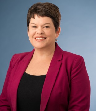 Headshot of a woman with a brown pixie cut, smiling, wearing a red blazer.