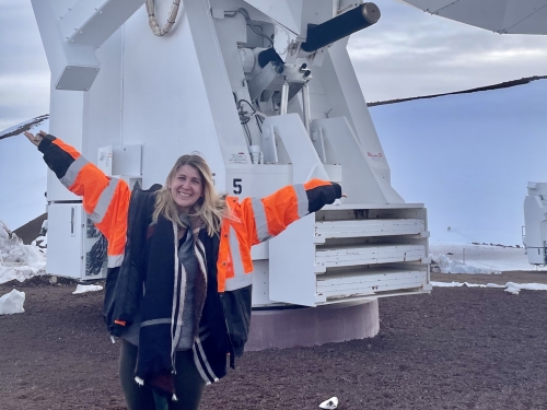 A blond woman stands with her hands up in front of an array.