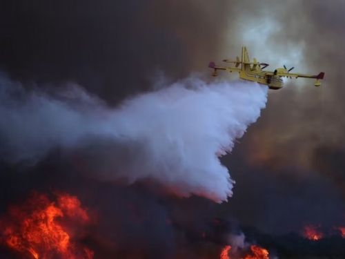 A plane dumps water onto a burning hillside