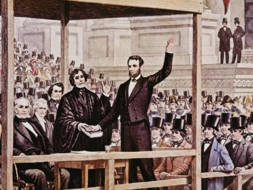 Two men stand on a wooden platform in front of a crowd of people. 