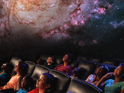 Kids sit in the planetarium theater.
