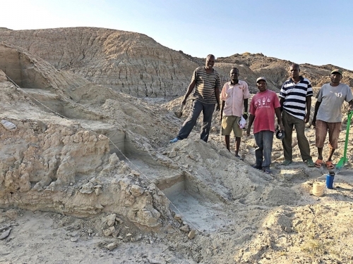 A group of men with plastic shovels stand in sandy, rocky area.