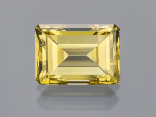Close-up of a singular yellow diamond, emerald cut, against a plain gray background.