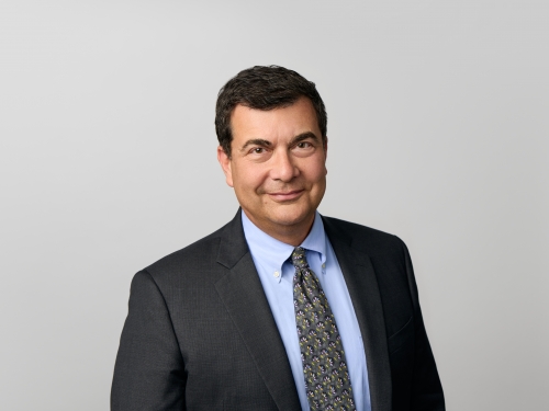 Man with short dark hair smiles with mouth closed, wearing a dark suit.