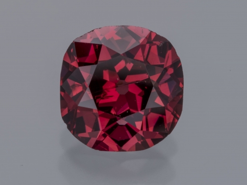 Close-up of a singular red diamong against a light gray background.