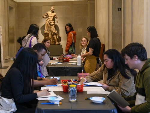 A group of visitors sit at tables making crafts in a gallery hall.