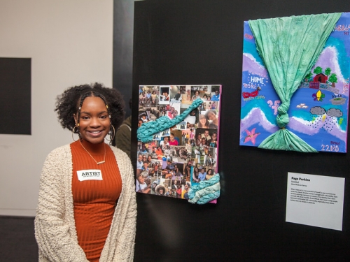 Young student stands in front of artwork on display