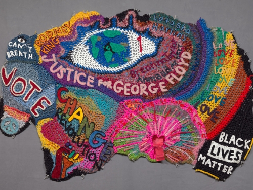 Crocheted multi-colored sculpture laying flat against grey background
