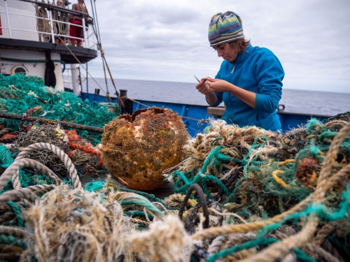 Person on a boat stands behind a close-up of trash