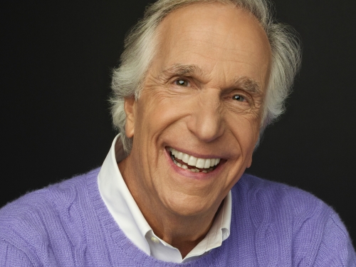 Headshot of white man smiling in a purple sweater and white collar.