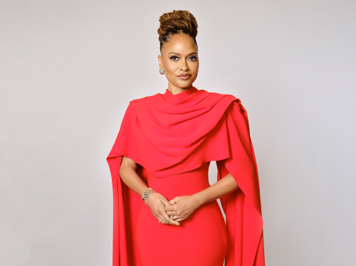 Woman wearing a red dress with a flowing shoulder cover.