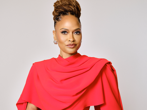 Woman poses for a picture wearing a red dress with a shoulder drape.
