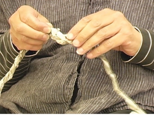 close-up of persons hands twisting long string together
