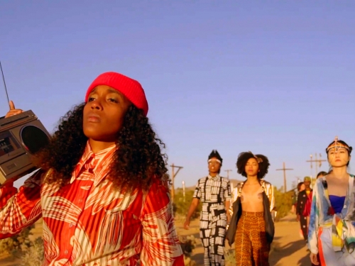 Woman in foreground carries boombox on her shoulder with 3 other women seen following behind her. Seen outdoors