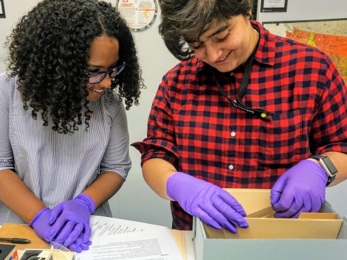 Two young adults smile as they peer into an archival box