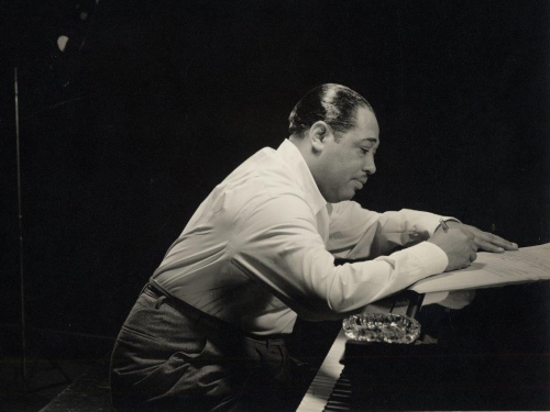 Duke Ellington in profile leaning over a piano