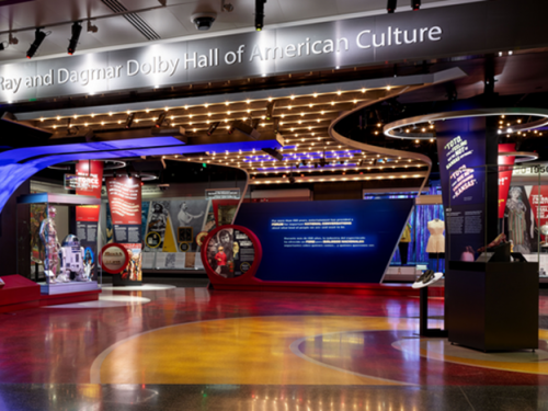 Entrance to brightly lit museum exhibit with object cases and wall text