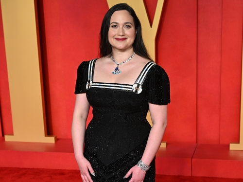Woman in a floor-length black dress poses for cameras on the red carpet.