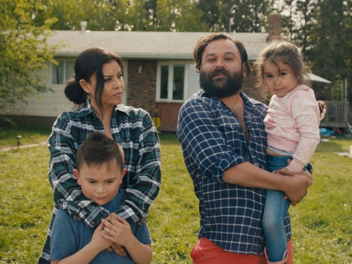 Photo of parents with their children in yard in front of small home
