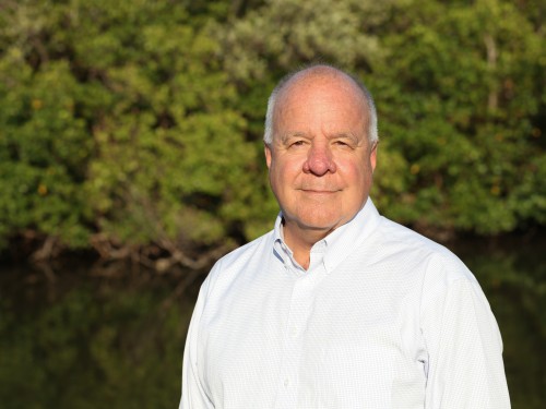 Man in a white button-up stands outside for a portrait photo.
