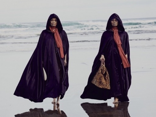 A pair of women in long black dress and headcoverings walk on reflective beach