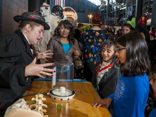 Woman in a costume speaks animatedly across a table to a group of young children.