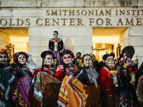 Photograph of people in traditional skull face painting and colorful clothing standing in a line.