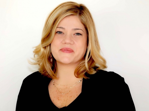 Woman with shoulder length blonde hair smiles with mouth closed.